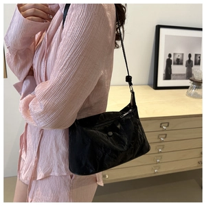 Vue latérale d'un sac d'épaule en cuir plissé noir porté par un mannequin en intérieur