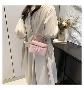 Side view of pink quilted vanity bag with chain strap worn by a woman in a white coat