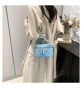 Detail of light blue quilted mini barrel bag with gold chain strap on trench coat