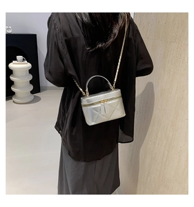 Detail of silver quilted handbag with metal chain strap and top handle in a lifestyle setting