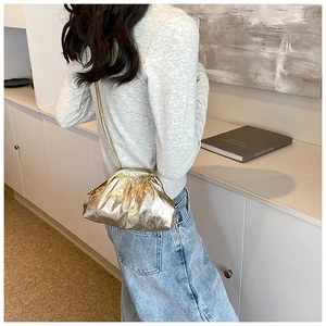 Detail of a metallic gold cloud-shaped pleated crossbody bag worn by a model