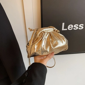 Detail of metallic gold cloud pouch bag featuring pleated leather and a thin shoulder strap