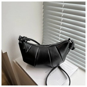 Detail of black pleated crescent bag with knot strap and metallic zipper on white stand