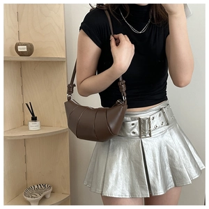 Detail of dark brown pleated dumpling bag with silver hardware and knotted strap on model