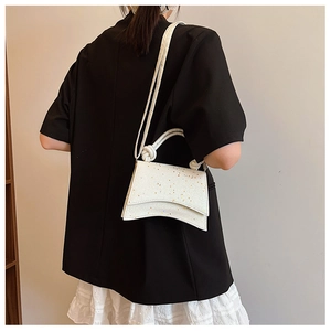 Detailed view of white sequined handbag with unique concave base and knotted handle