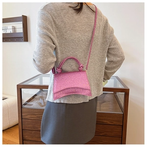 Pink sequin handbag with a curved base and knotted handle shown in a lifestyle setting