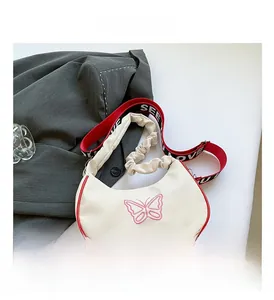 Détail du sac demi-lune blanc avec bordure rouge, broderie papillon et sangle logo