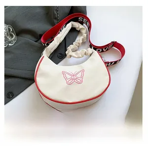 Détail du sac bandoulière en croissant avec broderie papillon rose et liseré rouge