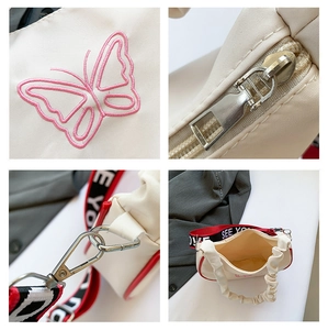 Gros plan sur la broderie papillon rose, zips argentés et bandoulière de sac en toile
