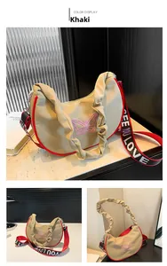 Détail du sac demi-lune kaki avec broderie papillon rose et liseré rouge contrasté