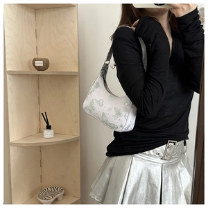 Detail of a minimalist half-moon shoulder bag with green butterfly print on a wooden stand