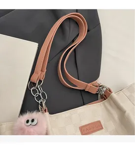 Close-up of beige plaid shoulder bag with pink leather strap and fashion label detail