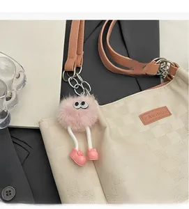 Detail of cream checkered tote bag featuring a cute pink plush monster bag charm