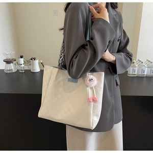 Detail of cream tote bag with checkerboard pattern, chain strap, and plush charm