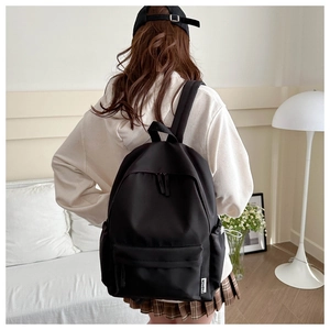 Close-up of a minimalist black nylon backpack featuring a white FASHION tag and side pocket
