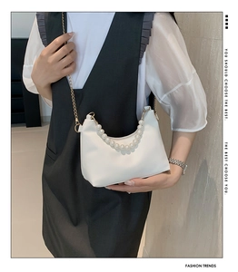 Detail of white half-moon bag with elegant pearl handle and gold chain strap in use