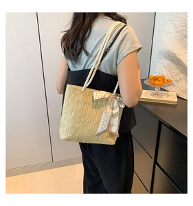 Detail of straw shoulder bag featuring a white rope handle and silk scarf decoration