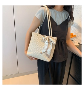 Close-up of beige straw tote bag featuring a heart print silk scarf bow and rope handles