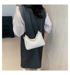 Detail of white moon bag featuring pearl handle and gold chain strap on model