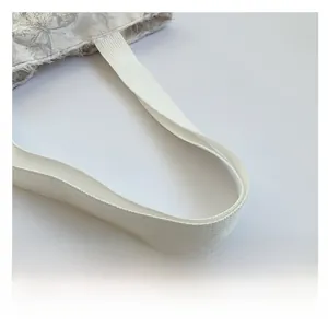 Detail of durable woven shoulder strap and intricate lace embroidery on a beige tote bag