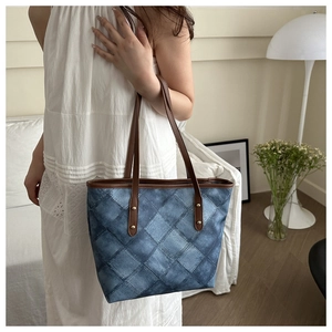 Detail of blue denim quilted tote bag with brown leather handles and gold metal rivets