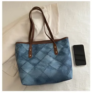 Detail of denim tote bag showing size compared to a smartphone on a beige fabric background