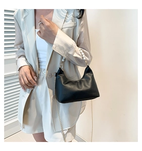 Detail of minimalist black faux leather bag featuring elegant pearl handle and gold chain