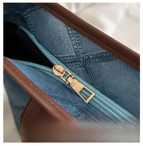 Detail of smooth metal zipper and brown leather trim on a blue denim tote bag