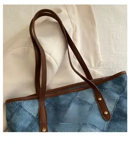 Close-up of blue denim patchwork tote bag with brown leather handles and gold rivets