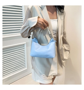 Detail of light blue hobo bucket bag with pearl handle and golden chain on model