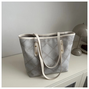 Detail of silver tote bag with cream straps and gold rivets on a minimalist cabinet