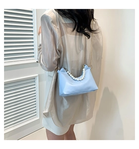 Light blue pearl chain bucket bag shown on shoulder against a minimalist white background