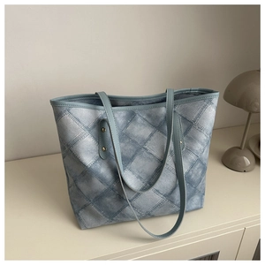 Close-up of light blue denim textured tote bag with quilted diamond pattern and gold rivets
