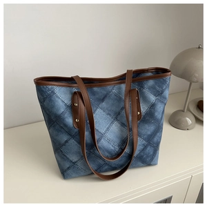 Detail of blue denim patchwork tote bag with brown leather straps and gold metal rivets