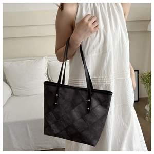Detail of black quilted tote bag with gold rivet accents and long shoulder straps