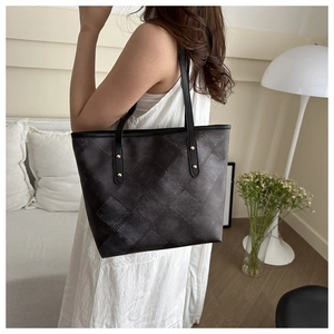 Detail of black textured tote bag with gold rivet accents and checkered leather pattern