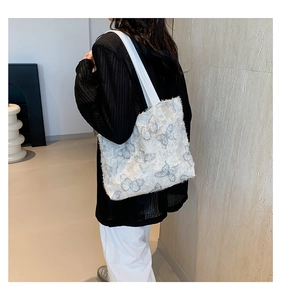 Detailed view of white tote bag featuring blue butterfly embroidery and textured lace fabric
