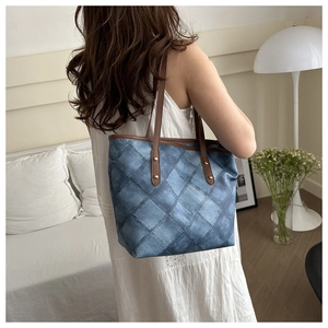 Detail of blue denim tote bag featuring diamond quilt patchwork and brown leather handles