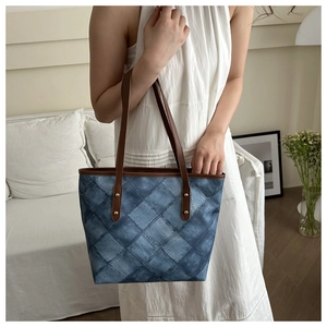 Detail of blue quilted denim tote bag with brown leather handles and gold rivets