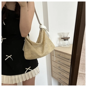 Detail of the woven straw tote bag with white leather strap and knot accent