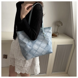 Detail of light blue tote bag with plaid texture and metal rivets in a home setting