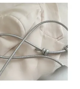 Detail of silver leather handbag with knotted strap resting on a beige suit jacket