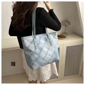 Detail view of large denim blue tote bag with quilted diamond pattern on female model