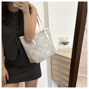 Detail of grey quilted tote bag with beige trim and secure metal rivet handles