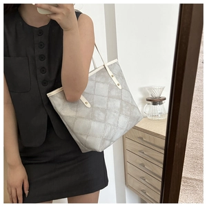 Close-up of light gray quilted tote bag with thin shoulder straps and metallic studs