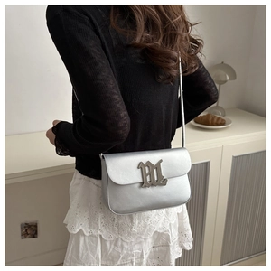 Silver metallic leather shoulder bag shown on model with gothic metal logo detail