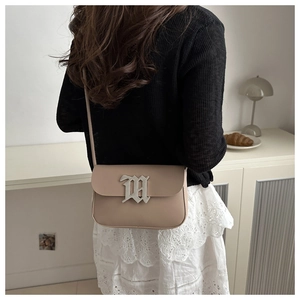 Detail of a beige flap bag with a large silver Gothic M buckle shown in a lifestyle setting
