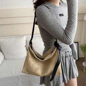 Handwoven straw tote bag with black leather shoulder strap and a hollow mesh hobo design