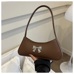 Detail of a dark brown leather baguette bag featuring a silver metal bow and slim handle