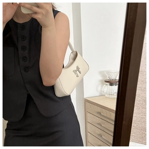 Primer plano de un bolso hobo blanco con un lazo plateado llevado por una modelo al espejo